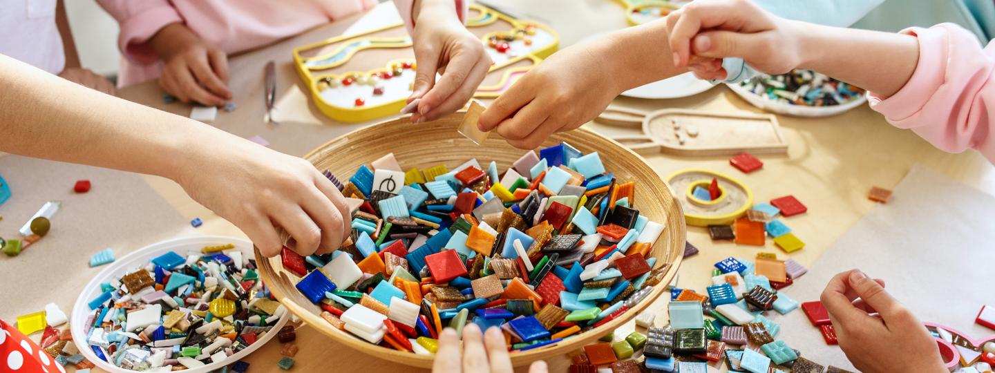 Conjunto de crianças em volta de uma mesa de cor bege cheia de pequenas peças de construção coloridas