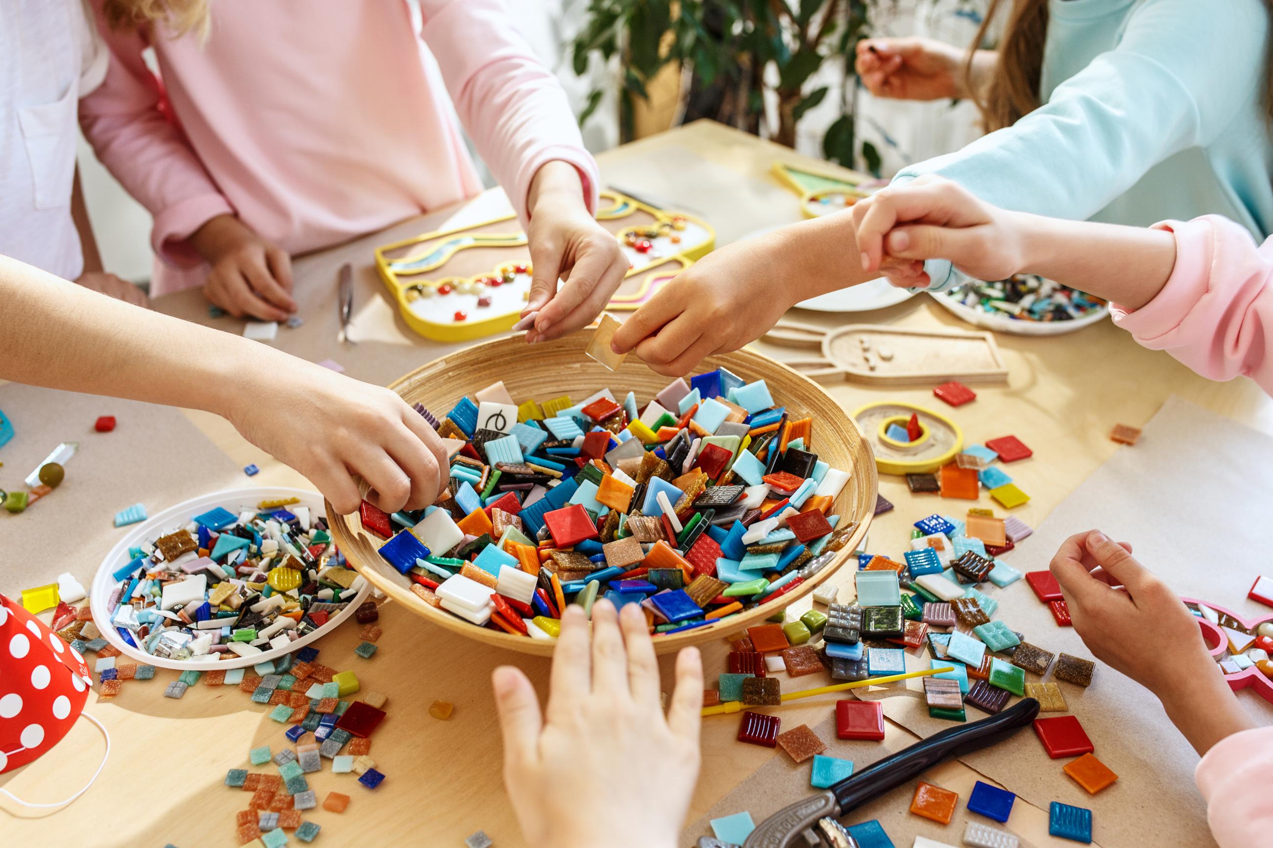 Conjunto de crianças em volta de uma mesa de cor bege cheia de pequenas peças de construção coloridas